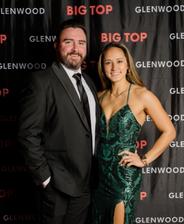 A man in a suit and a woman in a green dress pose together at an event with a "Glenwood Big Top" backdrop.