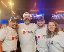 Four people wearing matching bowling-themed shirts, smiling together indoors.