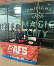 A man sits at an AFS info booth in front of a window reading "Birmingham The Magic City.