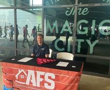 A man sits at an AFS info booth in front of a window reading "Birmingham The Magic City.