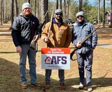 Three people holding rifles stand outdoors, smiling, next to an AFS sponsorship sign.