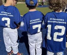 Three kids in blue baseball jerseys with numbers 7, 12, and 3, standing on a playground with a rubber surface.