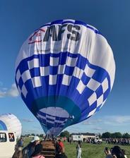 Blue and white checkered hot air balloon inflating at an outdoor event, with people gathered around.