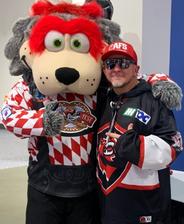 A person in sports gear poses with the Huntsville Havoc’s large, gray wolf mascot in a red and white jersey.