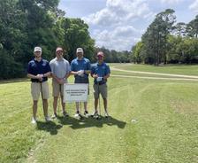 Four AFS teammates stand by a company sponsorship sign at the HBA of Metro Mobile President's Cup Golf Tournament