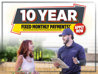 A woman talks to a man holding a clipboard under a sign that says "10 Year Fixed Monthly Payments. Apply Now.