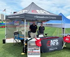 Two people stand under an AFS Sponsors tent at the Home Sweet Home Block Party, with brochures and red bags on the table.