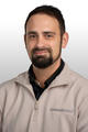 Meet The Team: Man with short dark hair and beard, in a beige “Groundworks” jacket, smiling at the camera against a white background.