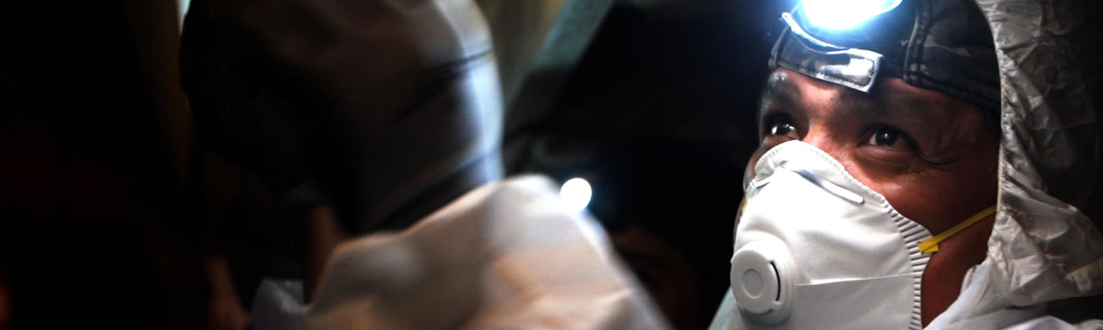 FSM crew member in crawlspace with mask and headlamp.