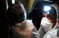 FSM crew member in crawlspace with mask and headlamp.