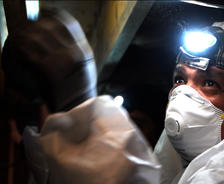 FSM crew member in crawlspace with mask and headlamp.