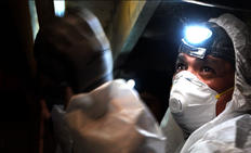 FSM crew member in crawlspace with mask and headlamp.