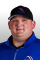 A person smiling while wearing a black cap and a blue jacket against a plain background.