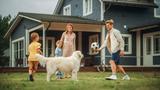 A family with two kids and a dog play soccer together in the yard in front of a house.