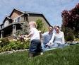 A family on a picnic blanket enjoys the outdoors; a child plays on the grass in front of a house with gardens.