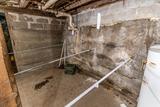 A damp basement with exposed pipes, concrete walls, and a water heater in the corner.