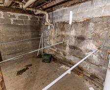 A damp basement with exposed pipes, concrete walls, and a water heater in the corner.