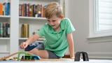 Young boy in a green shirt playing with toy cars and tracks on the floor in a bright room.