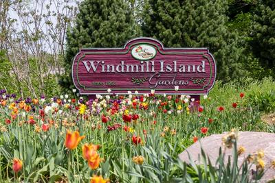 A "Windmill Island Gardens" sign stands behind colorful tulips and green trees.