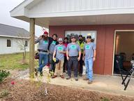 Seven people in work gear pose together on the porch of a house under construction.