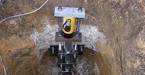 A hydraulic jack, often used alongside push piers, is installed in a dug-out hole for support or lifting.