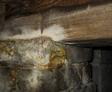 Close-up of stone and wood foundation with visible mold growth on surfaces, highlighting moisture problems in a crawl space.