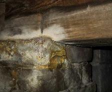 Close-up of stone and wood foundation with visible mold growth on surfaces, highlighting moisture problems in a crawl space.