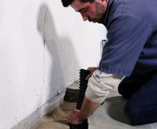 A man kneels, expertly installing waterproofing material along a basement wall, guarding against the 5 ways water enters your basement, ensuring a dry and secure foundation.