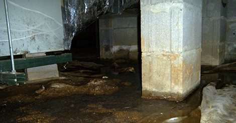 Flooded basement with puddles and dirt on the floor, surrounded by concrete support beams, often indicates subtle crawl space problems lurking beneath the surface.