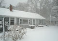 A house and yard covered in heavy snow during a winter snowstorm with trees in the background.