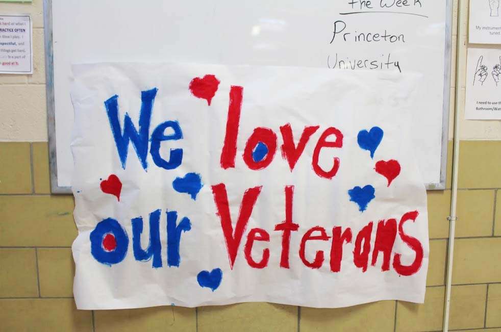 Handmade sign with red and blue letters reads "We love our Veterans," with hearts surrounding the text, beautifully capturing our heartfelt Veterans Day tribute in Norfolk, VA in 2015.