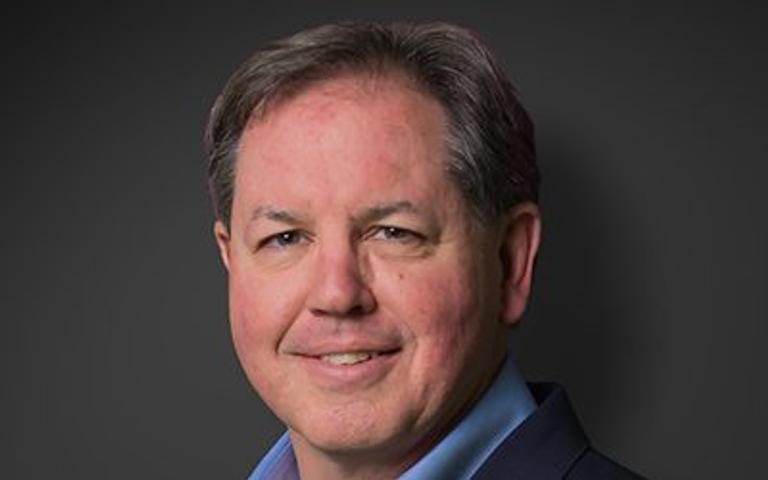Steve Frey, recently appointed by JES, smiles confidently in a suit against a dark background.