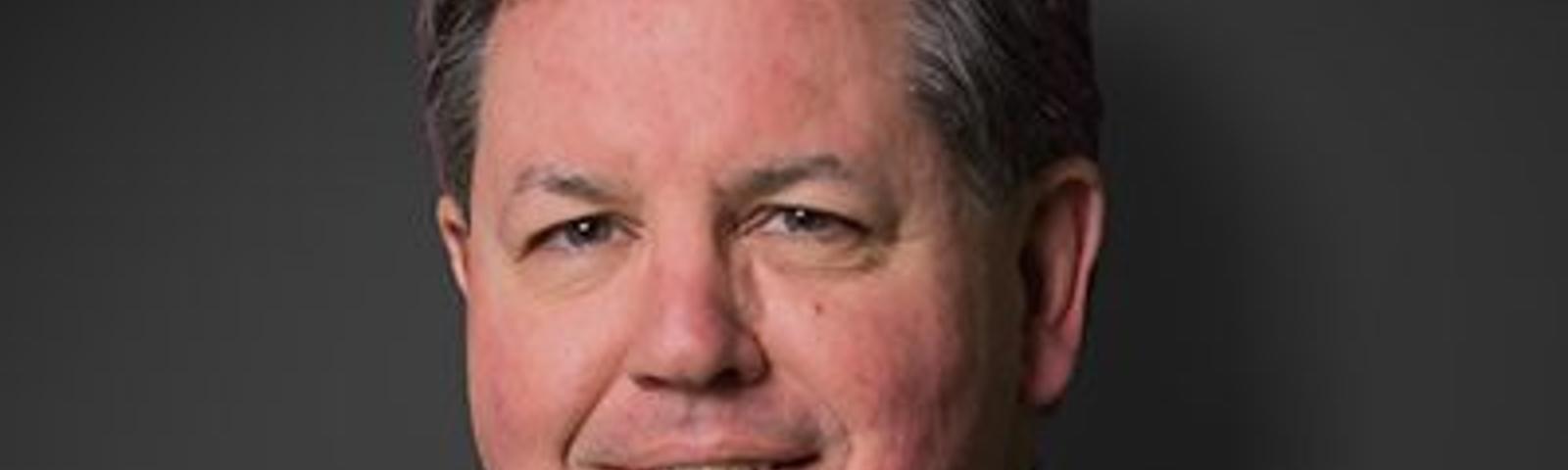 Steve Frey, recently appointed by JES, smiles confidently in a suit against a dark background.