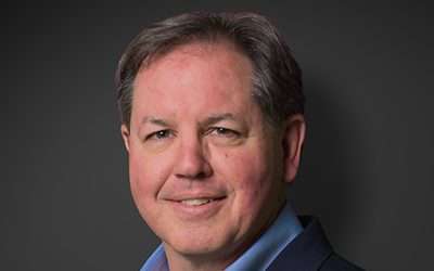 Steve Frey, recently appointed by JES, smiles confidently in a suit against a dark background.