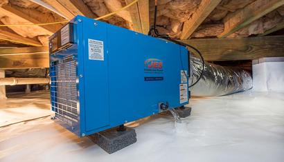 A blue crawl space dehumidifier runs beneath plastic sheeting and insulation, highlighting proper crawl space dehumidifier installation.