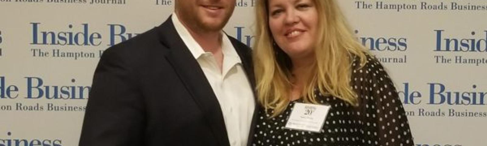 A man in a suit and a woman in a polka dot blouse channel the Roaring 20s as they pose confidently in front of an "Inside Business" backdrop.