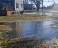 Large puddle of water covering a grassy yard near a house on a sunny day.