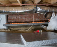 crew member installs crawl space insulation on walls in a crawl space