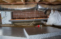 crew member installs crawl space insulation on walls in a crawl space