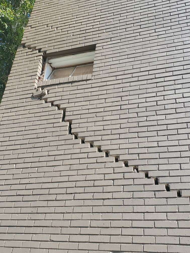 Cracked brick wall with horizontal zigzag pattern running from window to corner.