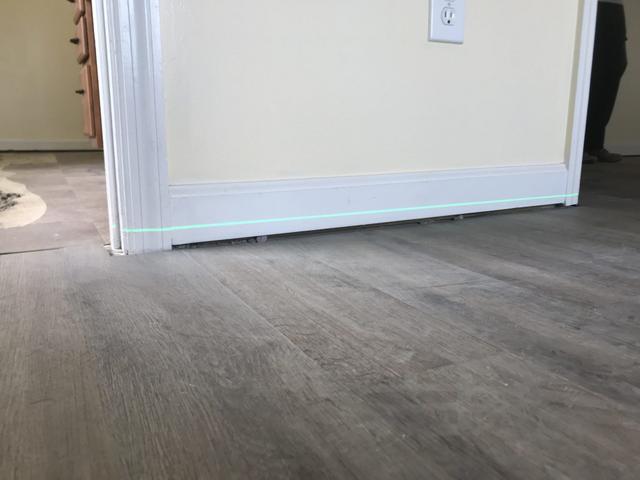 Close-up of a partially installed door, slightly ajar, with a visible green laser line on the hardwood floor—perfect for aligning steps if you're wondering how to fix sagging floors.
