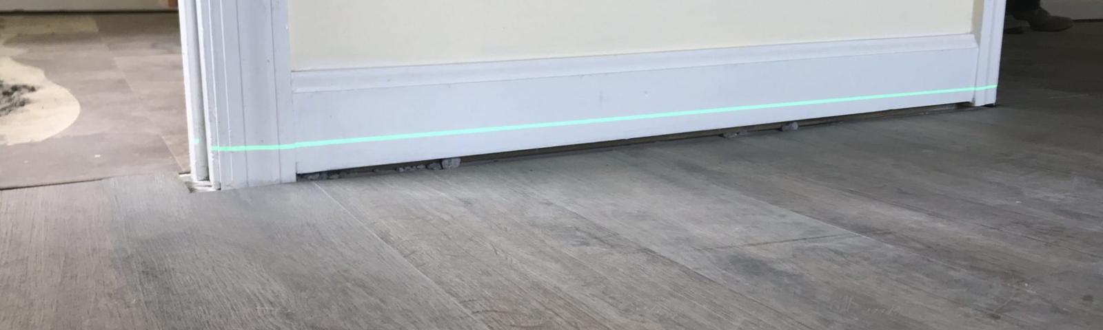 Close-up of a partially installed door, slightly ajar, with a visible green laser line on the hardwood floor—perfect for aligning steps if you're wondering how to fix sagging floors.