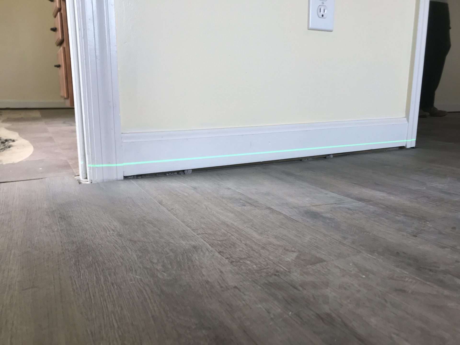 Close-up of a partially installed door, slightly ajar, with a visible green laser line on the hardwood floor—perfect for aligning steps if you're wondering how to fix sagging floors.