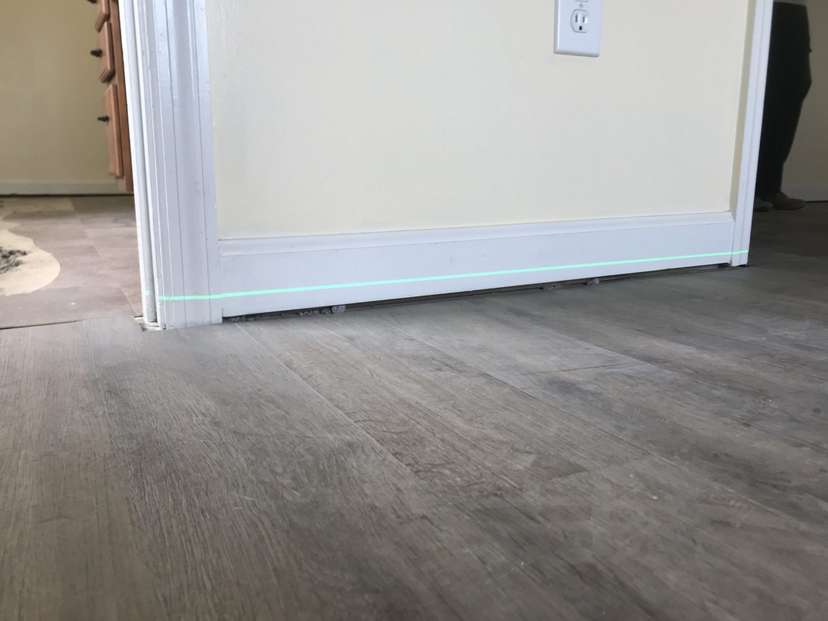Close-up of a partially installed door, slightly ajar, with a visible green laser line on the hardwood floor—perfect for aligning steps if you're wondering how to fix sagging floors.