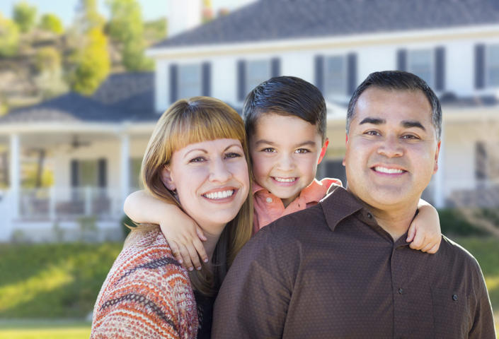 Smiling family of three posing together in front of a house.