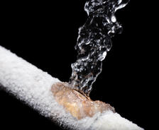 Water bursts from a frozen pipe covered in frost against a black background.