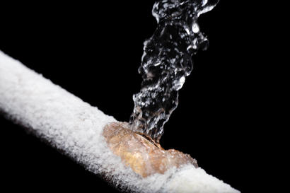 Water bursts from a frozen pipe covered in frost against a black background.