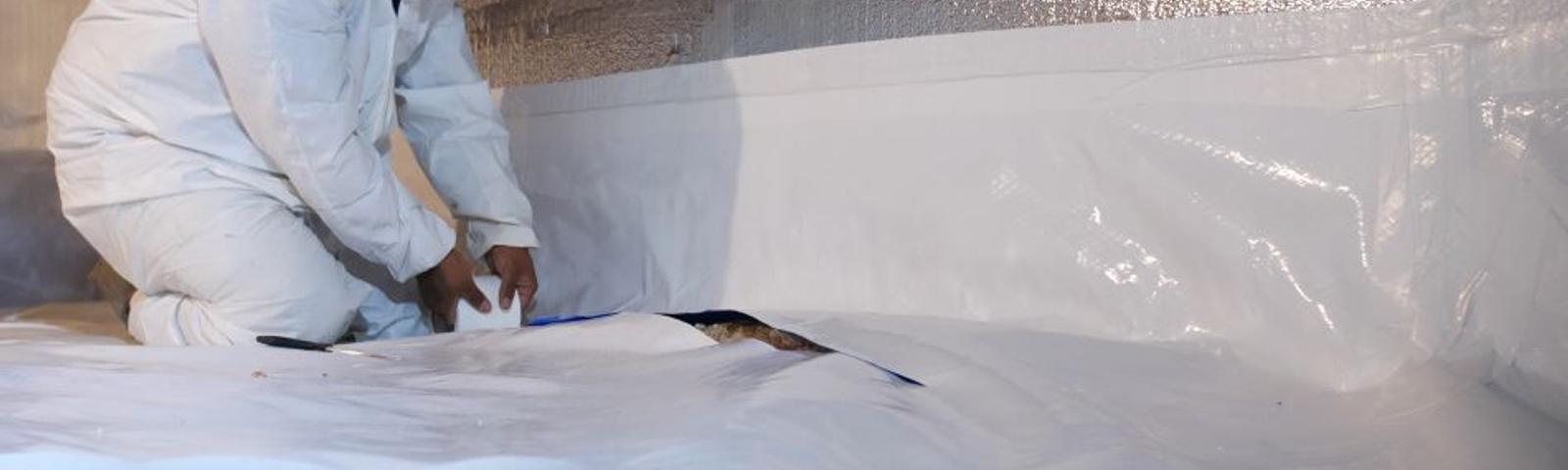 crew member installing crawl space encapsulation materials including wall insulation and a vapor barrier