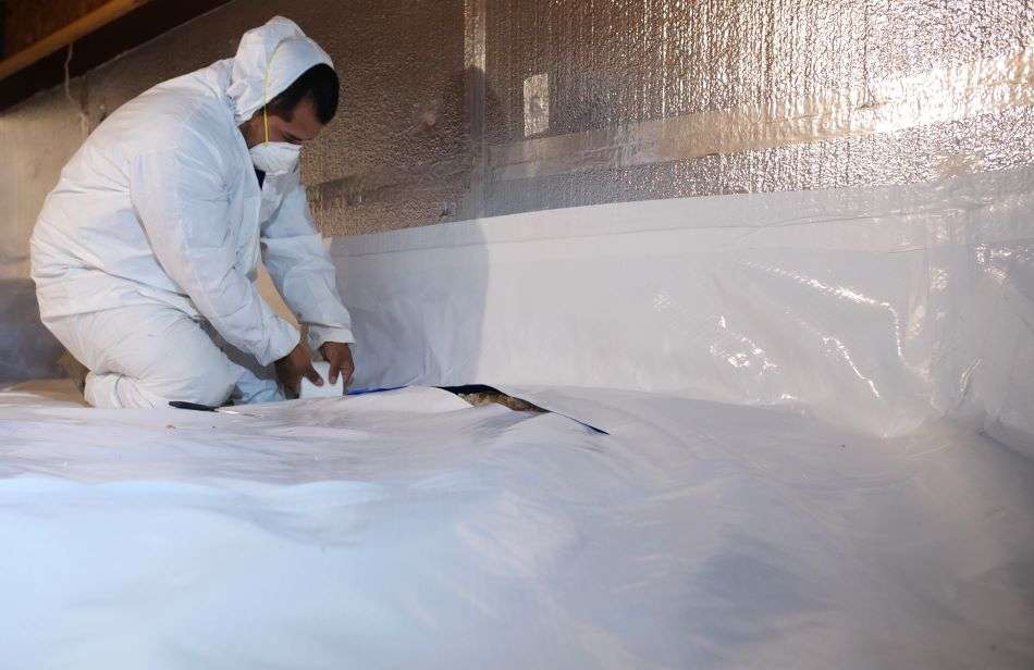 crew member installing crawl space encapsulation materials including wall insulation and a vapor barrier