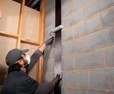 JES Foundation Repair crew member wearing face mask and gloves installing carbon fiber strap to a block basement foundation wall using a roller